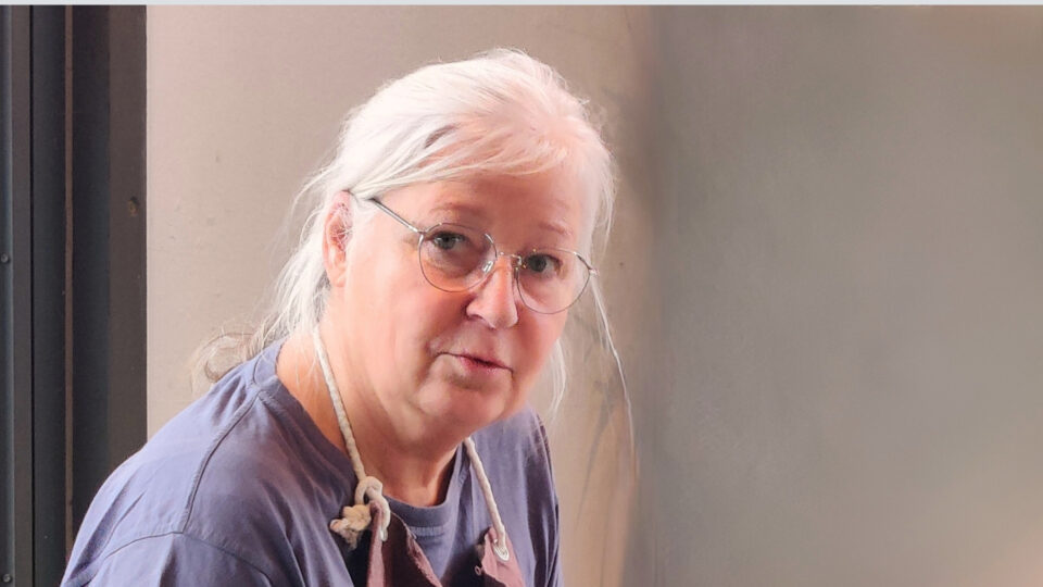 Petra Wild im Atelier – Künstlerin bei der Arbeit, mit fragendem Blick zur Kamera.