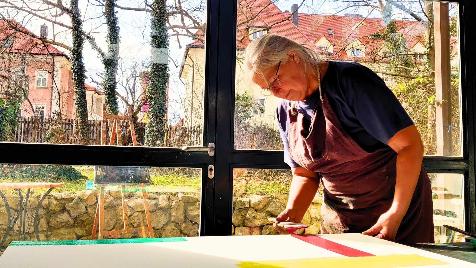 Petra Wild beginnt eine Arbeit in Lasurtechnik und hat einen breiten Pinsel mit roter Farbe in der Hand.